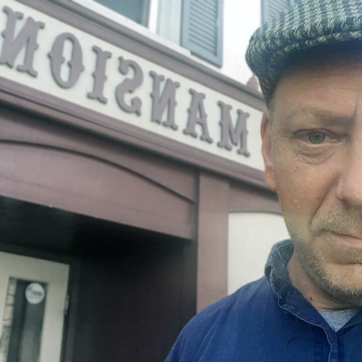 Photo of Russell Gragg in front of a sign that reads "Mansion."